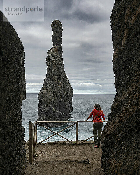 Woman stands at a railing at the landmark sea stack Ilheus da Ribeira da Janela on the island of Madeira  Portugal; Ribeira da Janela  Madeira  Portugal