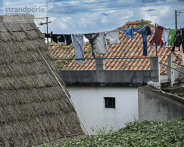 Clothesline between houses  roofs with clay roof tiles and thatching; Santana  Madeira  Portugal