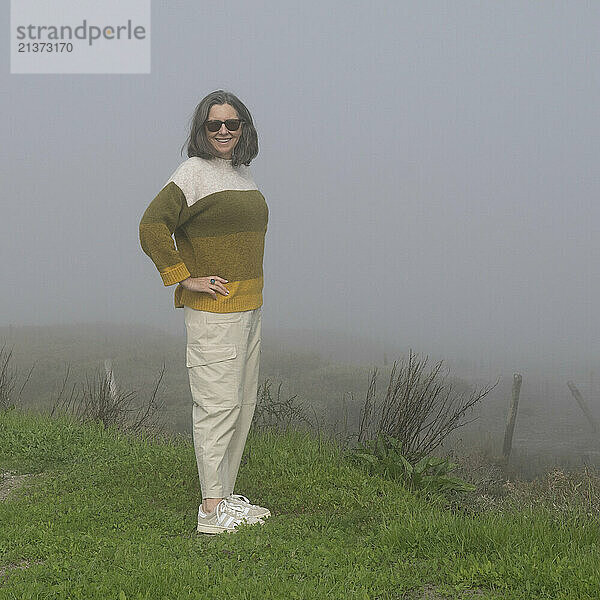 Mature woman wearing sunglasses stands on grass in the dense fog in Comporta  a freguesia and village in the municipality of Alcacer  in the old district of Setubal; Comporta  Alcacer  Setubal  Portugal