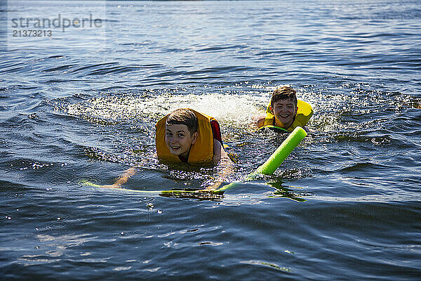 Two young brothers swimming and having fun at the lake during a family outing; Alberta Beach  Alberta  Canada