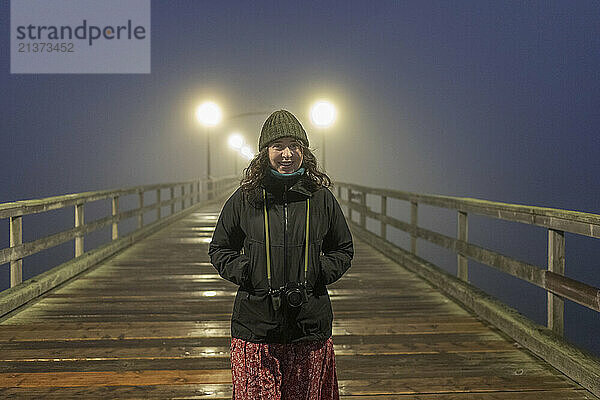 Portrait of a young woman smiling at the camera bundled up at night standing on a pier at White Rock; British Columbia  Canada