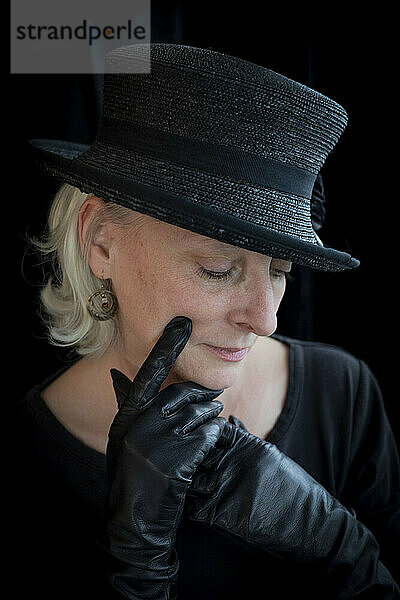 Portrait of a mature woman with black hat and leather gloves against a black background; Studio