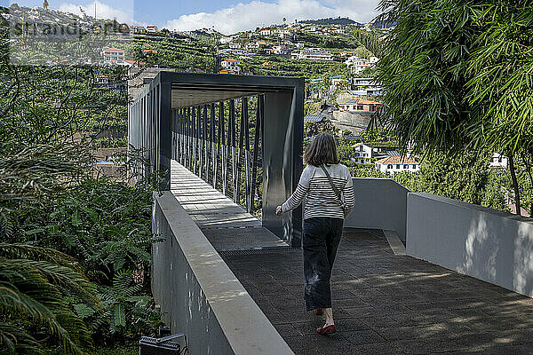 Woman walks towards an elevated walkway in the town of Ponta do Sol on the island of Madeira in Portugal; Ponta do Sol  Madeira  Portugal