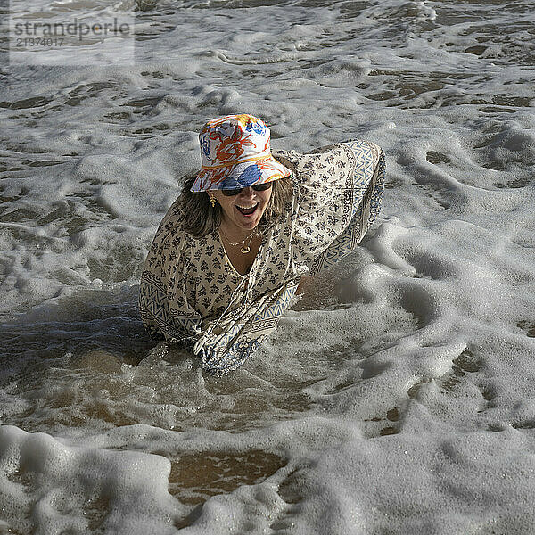 Woman enjoys time in the sea foam of the ocean surf on one of the Sagres Beaches on the Portugal coast; Sagres  Faro  Portugal