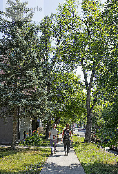 Two mid adult women walk down a neighbourhood sidewalk together; Winnipeg  Manitoba  Canada