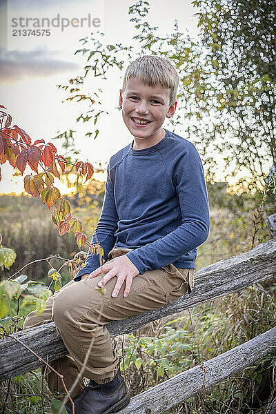 Close-up portrait of a boy sitting on a wooden fence  smiling at the camera in a rural setting in the Fall  Beckwith Township at Carleton Place in the Ottawa Valley; Ontario  Canada