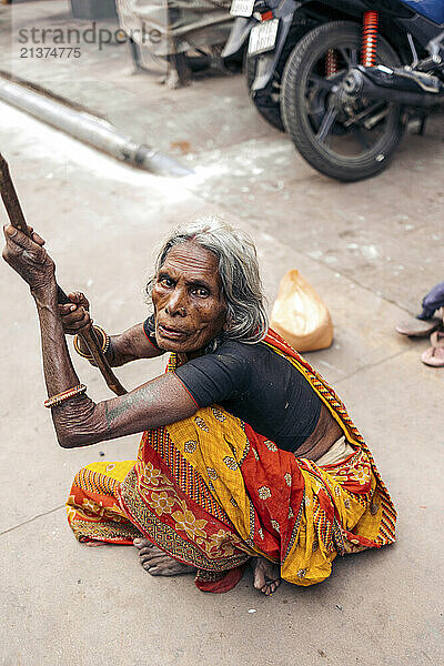 Senior woman sits on the ground with her walking stick; Varanasi  Uttar Pradesh  India