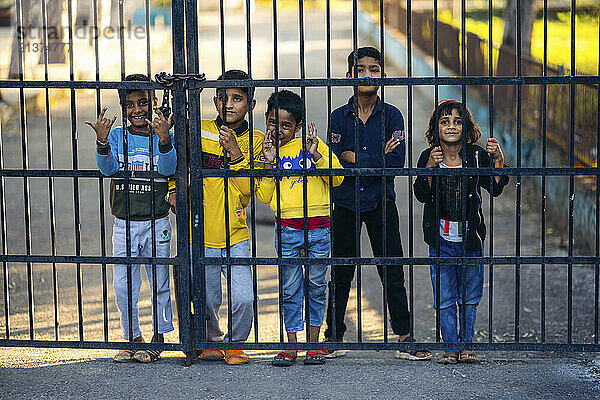 Kids stand looking through a metal fence and pose for the camera; Jammu  Jammu and Kashmir  India