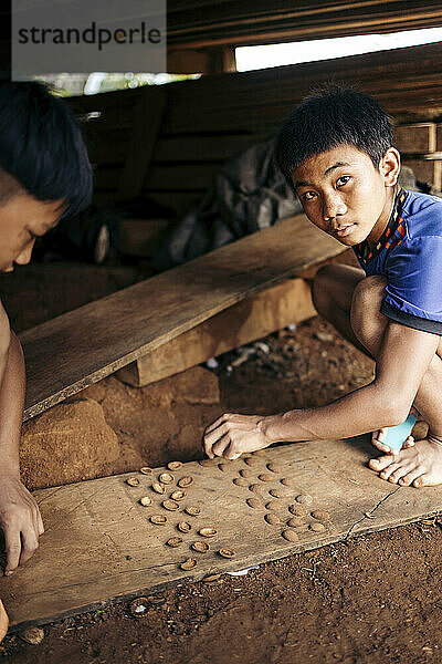 Two boys enjoy playing a game with shells on the ground in a village in Laos; Kok Phung Tai  Champasak Province  Laos