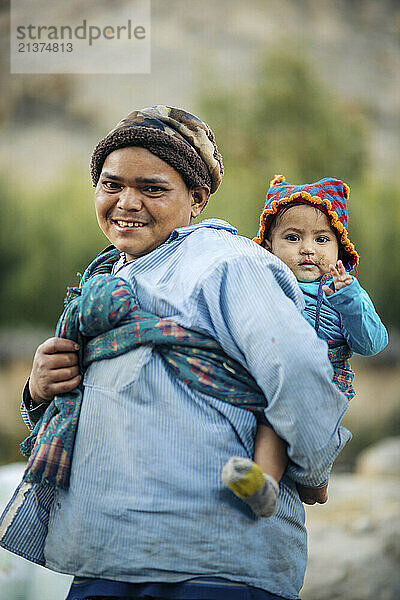 Mother walking with her young child in a sling on her back along the main road in the town of Tabo in Lahaul and Spiti district  India; Tabo  Himachal Pradesh  India