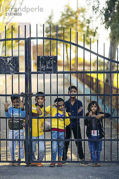 Kids stand looking through a metal fence and pose for the camera; Jammu  Jammu and Kashmir  India