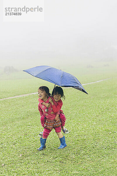 Two girls with an umbrella being silly on a rainy day; Ta So village  Moc Chau District  Son La  Vietnam