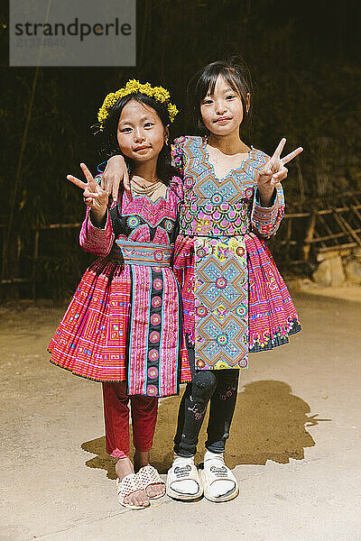 Hmong girls in traditional dress giving the peace sign  posing for the camera; Pa Co  Mai Chau  Son La  Vietnam