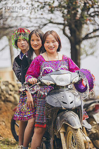 Three young Vietnamese women posing together on a motorcycle  wearing traditional dresses; Ban Nam Nghiep  Muong La  Son La  Vietnam