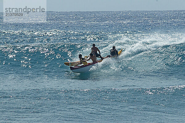 Young men paddling a canoe  riding over a wave in the pacific ocean  Hawaiian Islands; Hawaii  United States of America