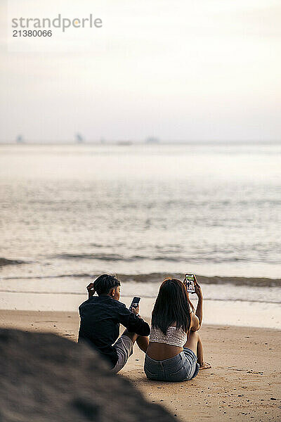 Young couple with their smart phones enjoy Ao Nang Beach at sunset; Krabi  Thailand