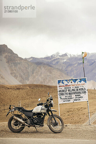 Motorcycle parked by a sign for Komic  the highest village in the world  Spiti Valley  Himachal Pradesh  India; Komic  Himachal Pradesh  India