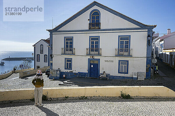 Woman stands looking at a blue and white house in the coastal town of Sines in the Alentejo region of Portugal; Sines  Setubal  Portugal