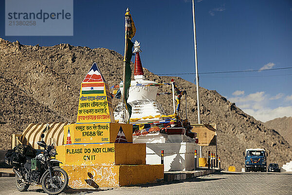 Chang La mountain pass with a motorcycle parked beside a high altitude marker and buddhist flags in the background in Ladakh  India; Ladakh  India