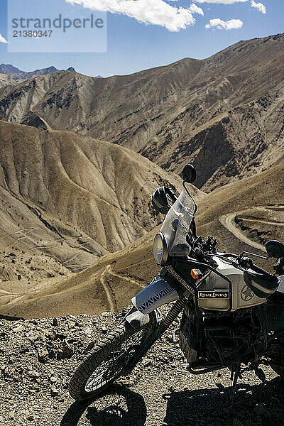 Motorcycle sits along the roadside with a view of the rugged terrain and winding road along the mountainside at Zanskar Valley in Ladakh  India; Ladakh  India