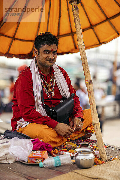 Hindu man sits under an umbrella with offerings in Varanasi  India; Varanasi  Uttar Pradesh  India