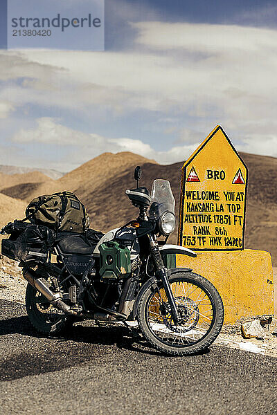 Motorcycle parked along Kaksang La mountain pass at a summit sign and high altitude marker in Ladakh  India; Ladakh  India