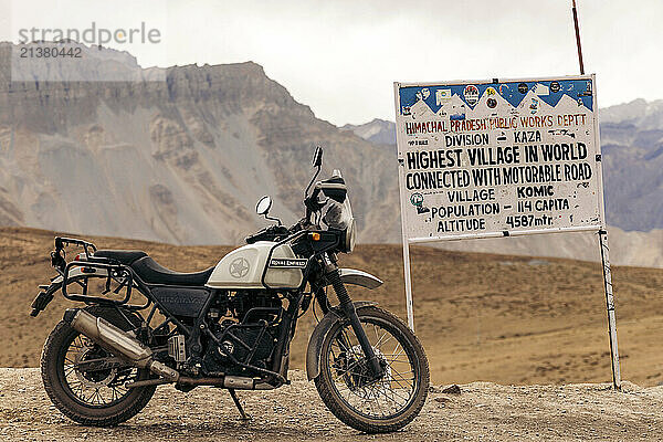 Motorcycle parked by a sign for Komic  the highest village in the world  Spiti Valley  Himachal Pradesh  India; Komic  Himachal Pradesh  India