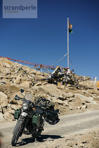 Motorcycle parked along Wari La mountain pass with buddhist prayer flags and the national flag of India in Ladakh; Ladakh  India