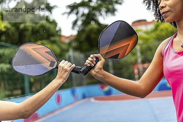 Cropped close-up photo of multiracial women clashing pickelball rackets before playing together