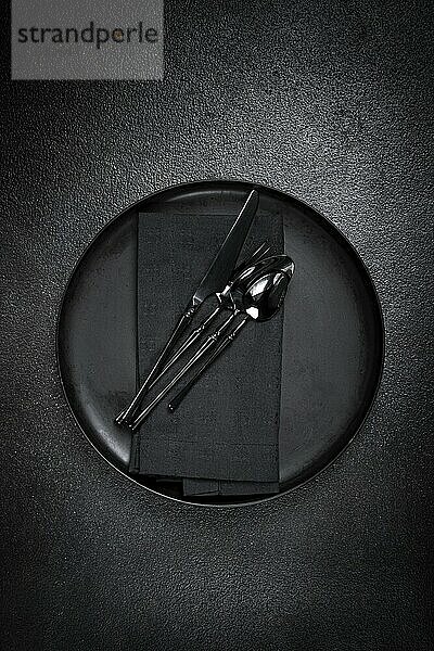 Food background  with an empty black plate  black cutlery  with a napkin  on a black background  table setting  top view  no people