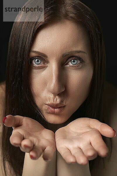 Adult woman blowing lips send air kiss over palms to her boyfriend and looking at camera. Pretty 40-year-old woman with gray eyes demonstrates good feelings. Front view  studio shot black background