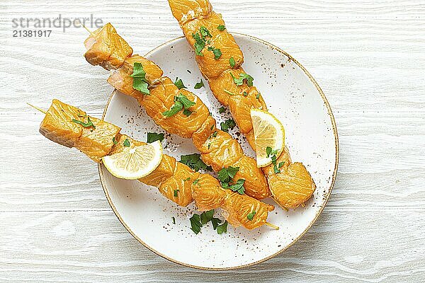 Grilled barbecue salmon skewers seasoned with green parsley and lemon on ceramic plate on white wooden rustic table background top view  healthy eating  food photography  food photography