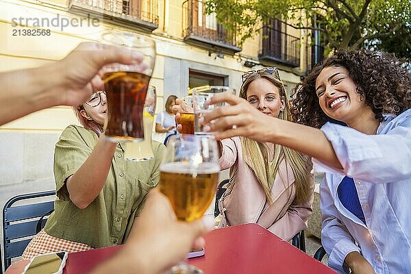 Group of happy friends toasting with beer sitting on outdoor terrace in the city during sunet