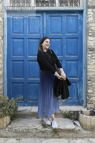 Young happy Caucasian woman posing and smiling in front of a blue door. Cheerful people outdoor