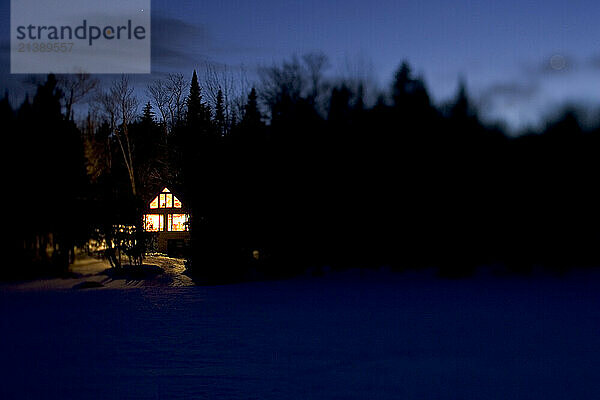 The lights of a lakeside cabin glow on a clear night in Maine.