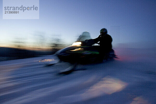 A snowmobiler speeds down a trail at dusk in Maine.