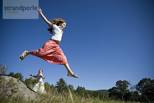 Colorfully dressed girls jump through the air in a green field near Bethel  Maine.