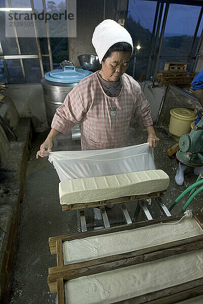 Kazuko Uezu  age 65  makes tofu before dawn in her small shop in the village of Hedo. Despite 50 years of practice every batch tastes slightly different says Kazuko who rises at 4-am seven days a week to make tofu. Traditional methods and a small production produces subtle variations in every batch despite the fact that tofu has only two ingredients  salt water and soy beans. Kazuko get the salt water from the East China Sea (just down the road from her house) but the soybeans come from America. Okinawan centenarians eat tofu daily and it is believed the high flavanoid content in tofu contributes to their longevity. Flavanoids are known to fight breast and prostate cancer and believed to combat heart disease.