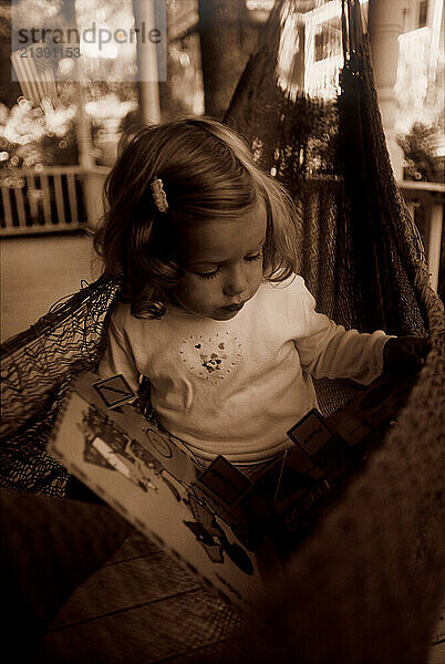 A young girl reads a picture book at her summer cottage in Bayside  Maine on Penobscott Bay. (releasecode: DM_MR1039)