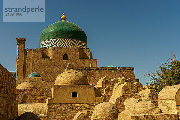 KHIVA  A large building with a green dome sits in front of a blue sky. The building is surrounded by many small domes  giving it a unique and intricate appearance