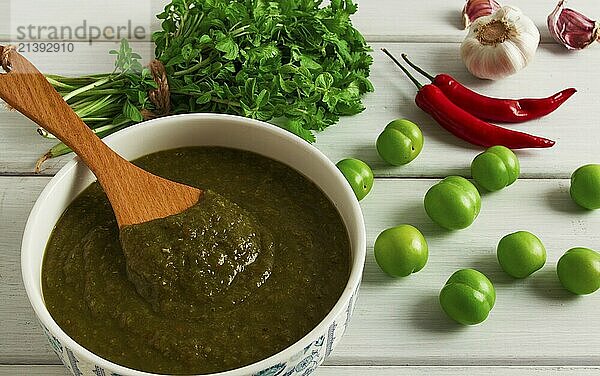 Tkemali sauce  traditional Georgian cuisine  green cherry plum  with ingredients for sauce  cilantro  mint  hot pepper  garlic  on a white wooden table  close-up  rustic  food background  no people  selective focus  sauce  green sauce  tkemali  georgian cuisine  homemade