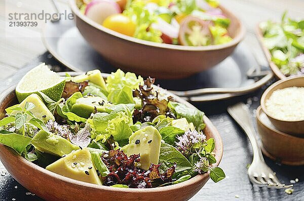 Clay dish with salad of avocado  green and violet lettuce  lamb's lettuce and oregano flowers on slate stone tray with soy sauce lime and sesame aside