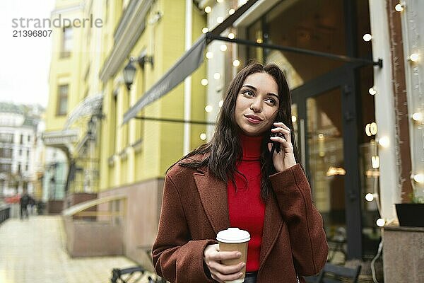 Business woman uses mobile phone on the street and drink coffee