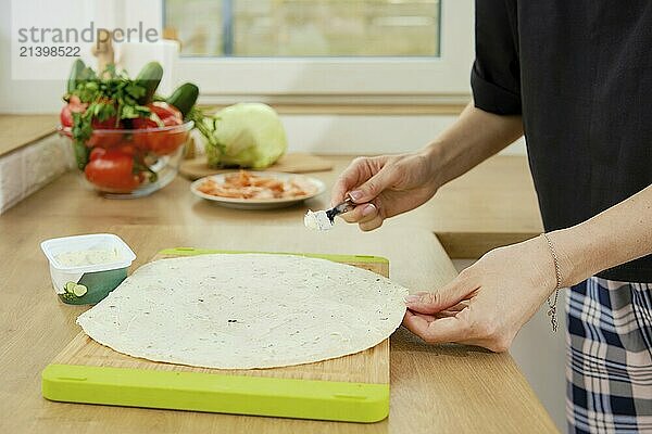 Closeup view of female hands applying cream cheese to lavash with spreader knife  preparing a snack