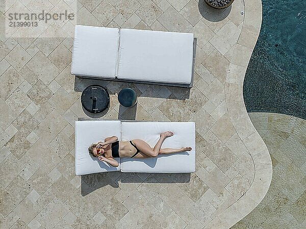 A gorgeous blonde bikini model enjoys a day off at home lounging by the swimming pool