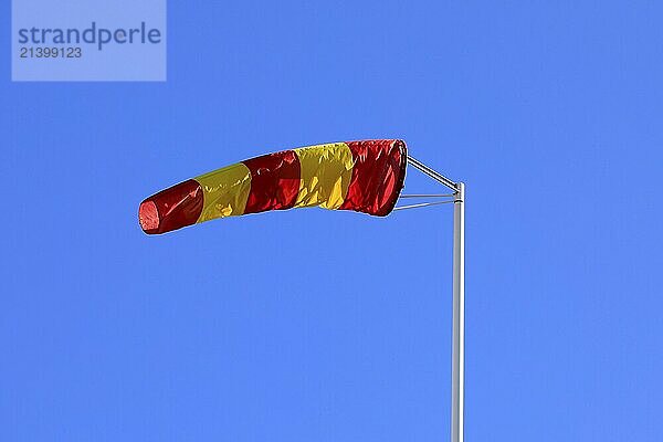 Yellow and red striped windsock or wind cone against clear blue sky  indicating wind direction and force. Copy space for your text