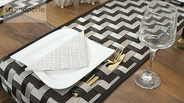 Elegant table setting with gold cutlery on a checkered placemat and a wine glass