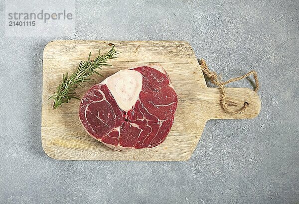 A shank on the bone  raw meat for ossobuco  on a wooden chopping board  with a branch of rosemary  top view  no people.