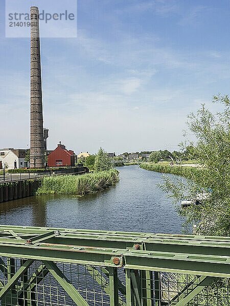 Industrial landscape with high chimney and river under blue sky  ulft  gelderland  netherlands