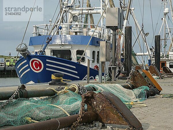 A blue fishing boat lies in the harbour  surrounded by nets and anchors on the cobblestones  dornumersiel  dornum  east frisia  germany